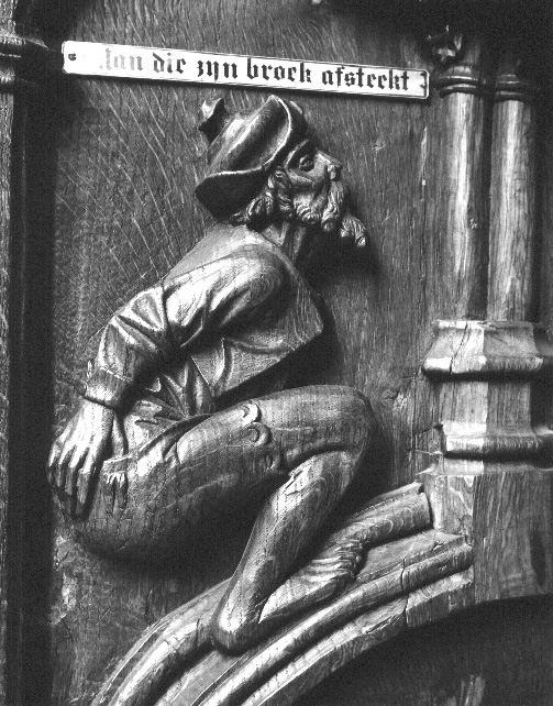 Koorbanken, detail: gehurkte man die met rechterhand zijn broek omlaag trekt