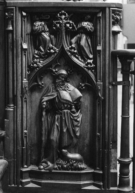 Koorbanken, detail: de kluizenaar H. Antonius met klokje, boek, T-staf, vlammen en varken