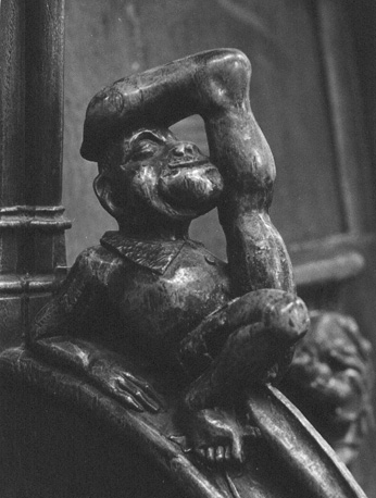 Koorbanken, detail: knop met liggende man met een been opgestrekt en ander (met grote voet) omhoog