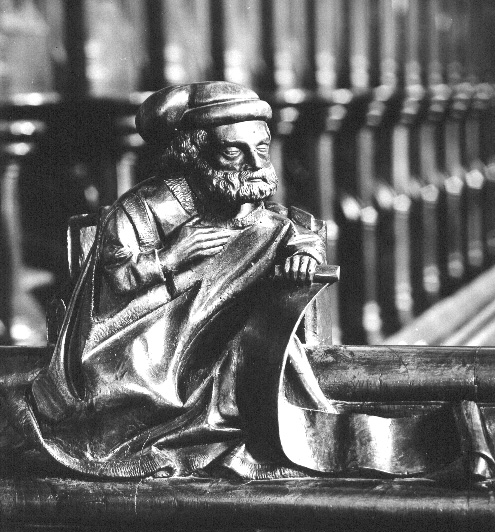 Koorbanken, dekstuk: zittende figuur met banderol: profeet?