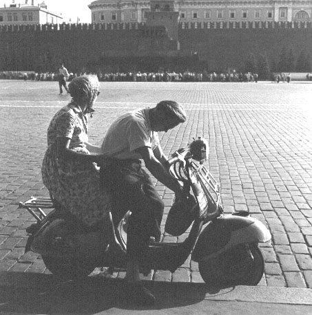Man en vrouw op scooter; op achtergrond: Kremlin, veel mensen wachtend voor ingang van Lenin-mausoleum