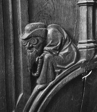 Koorgestoelte, wang: zittend figuur met hoed, bril, baard en bidsnoer