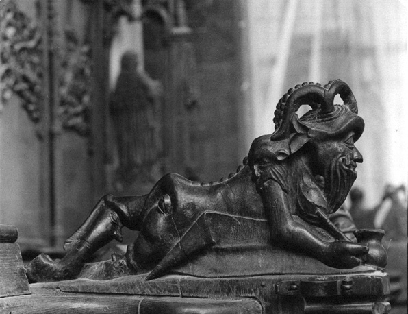 Koorgestoelte, detail: liggend figuurtje,  voorstelling van duivel met attributen van de bok: baard, hoorns en bokkepoten (zijaanzicht)