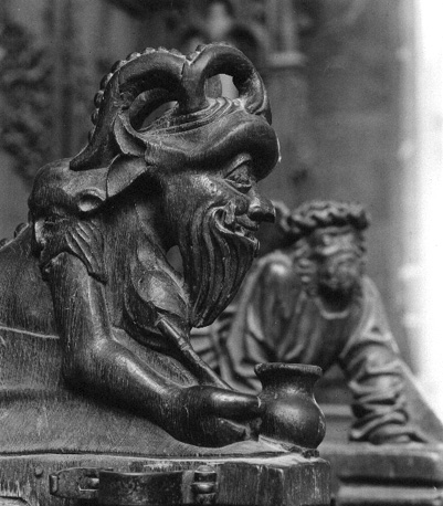 Koorgestoelte, detail: liggend figuurtje,  voorstelling van duivel met attributen van de bok: baard, hoorns en bokkepoten (zijaanzicht, detail)