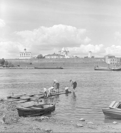 Zicht op stadsmuur, verschillende kerktorens achter de muur, vrouwen doen de was in de rivier