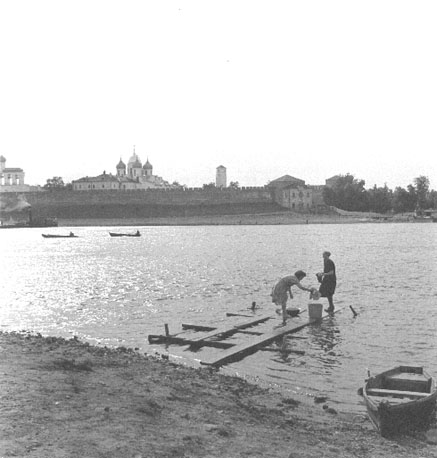 Zicht op stadsmuur aan de rivier, verschillende kerktorens achter de muur, vrouwen doen de was