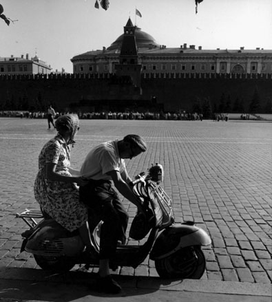 Man en vrouw op scooter; op achtergrond: Kremlin, veel mensen wachtend voor ingang van Lenin-mausoleum
